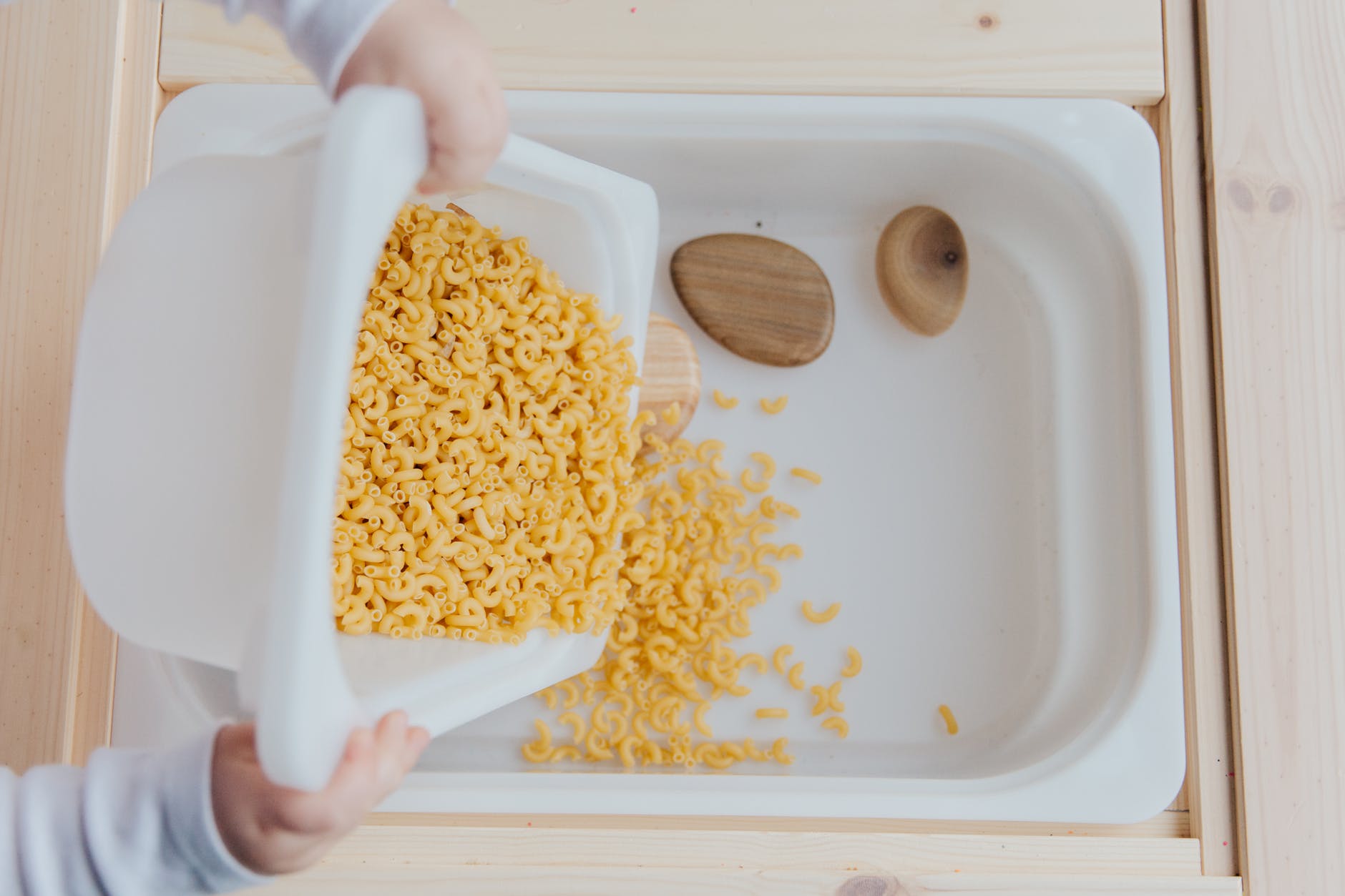 unrecognizable crop kid adding raw pasta to white container